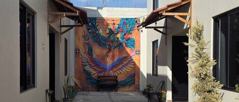 A courtyard with a mural, potted plants, and a bench.