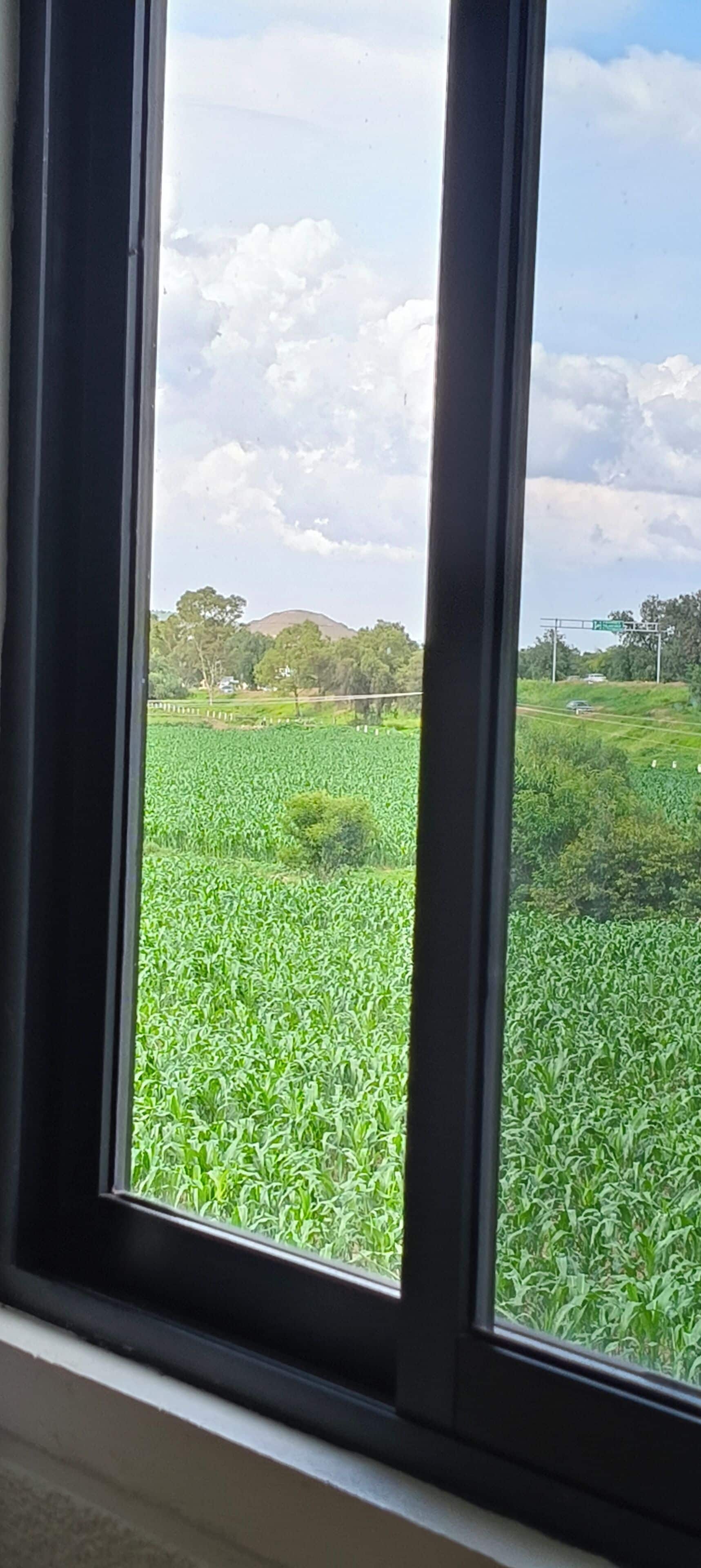 Vista a través de una ventana que muestra un campo verde, una carretera y un cielo nublado.