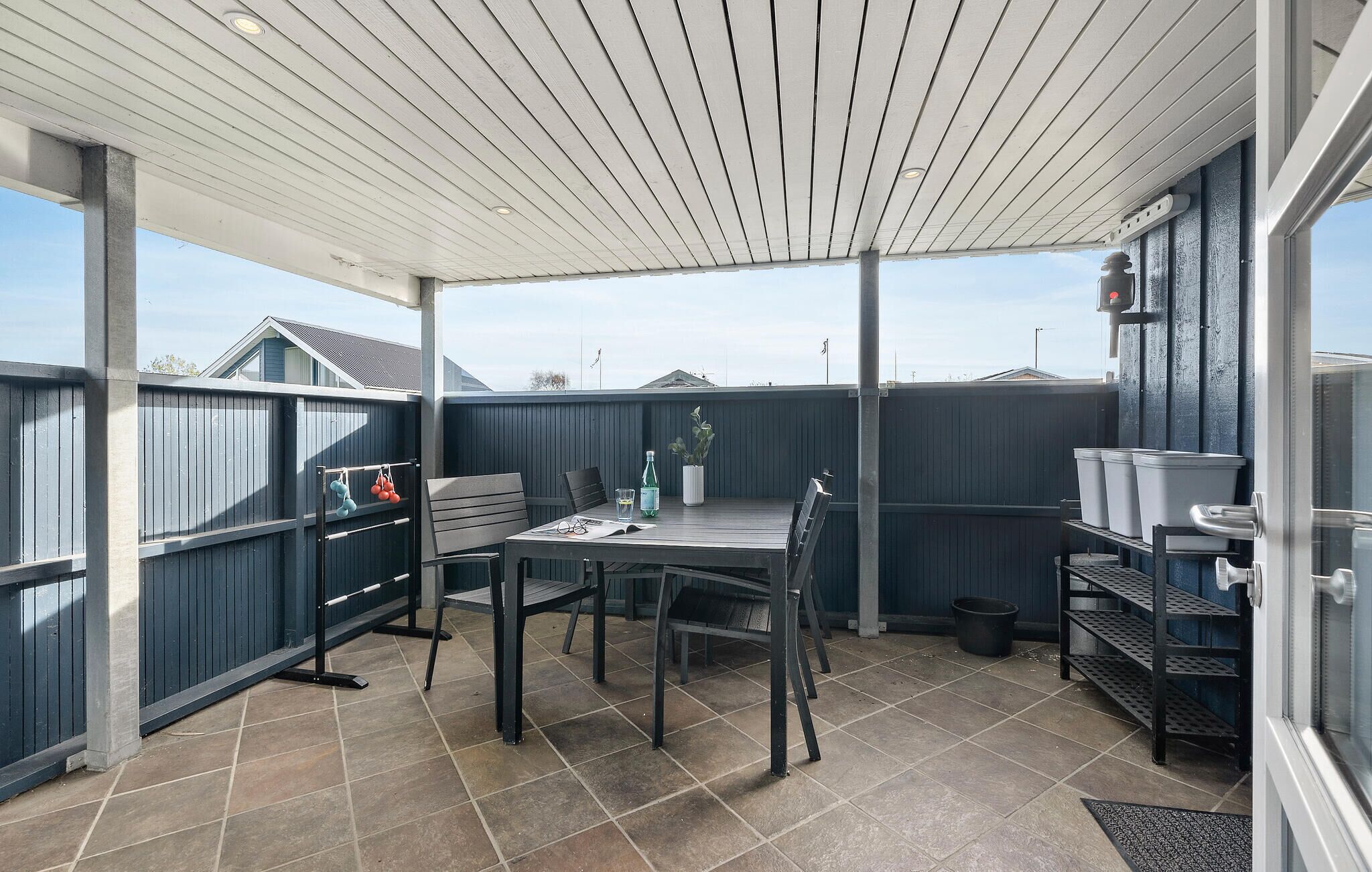 A covered patio area with a table and chairs, a potted plant, and storage shelves.