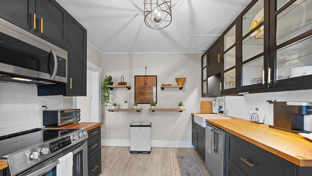 Cocina moderna con armarios negros, electrodomésticos de acero inoxidable y encimeras de madera.