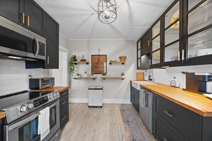 A modern kitchen with black cabinets, stainless steel appliances, and wooden countertops. - Deja Blue Bungalow | Pet-Friendly Asheville Monthly Rental | Two Fenced Yards (Asheville)