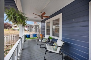 A covered porch with a ceiling fan, a bench with cushions, and a table with chairs. - Deja Blue Bungalow | Pet-Friendly Asheville Monthly Rental | Two Fenced Yards (Asheville)