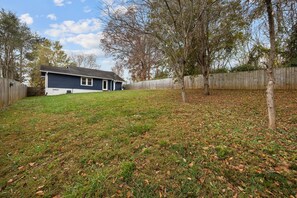 A residential backyard with a house, a wooden fence, and trees. - Deja Blue Bungalow | Pet-Friendly Asheville Monthly Rental | Two Fenced Yards (Asheville)