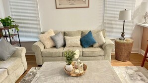 A living room with a beige sofa, a coffee table with decorative items, and a framed beach painting on the wall.