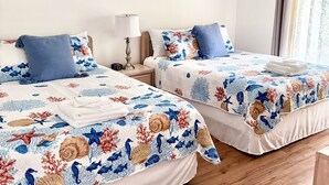 A hotel room with two beds, each with a floral bedspread, a ceiling fan, and a window with curtains.