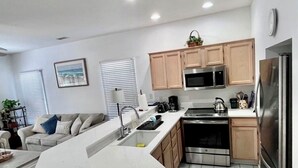 A modern kitchen with a central island, wooden cabinets, stainless steel appliances, and a dining area with a sofa and coffee table.