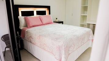 A neatly made bed with a white and pink patterned bedspread, a black headboard, and a small bedside table with a lamp.