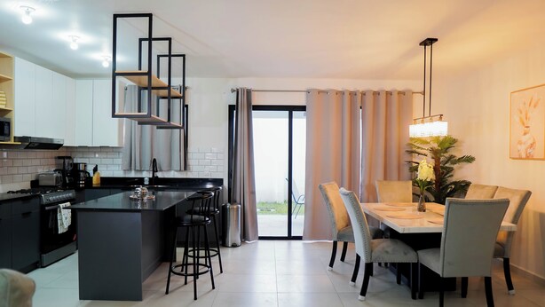 A modern kitchen with a central island, bar stools, and a dining area with a table and chairs. - Beautiful Modern Home in Res San Andres  (San Miguel)