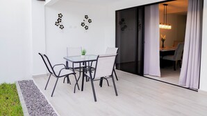 Un espace repas extérieur moderne, avec une table et des chaises en verre, une petite plante en pot et des éléments décoratifs sur le mur.