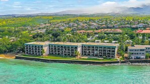 Un complejo turístico con varias edificaciones, una playa y un paisaje verde exuberante al fondo.