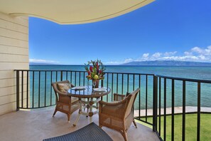 A balcony with wicker furniture, a glass table, and a vase of flowers. - Kahana Reef (Lahaina)