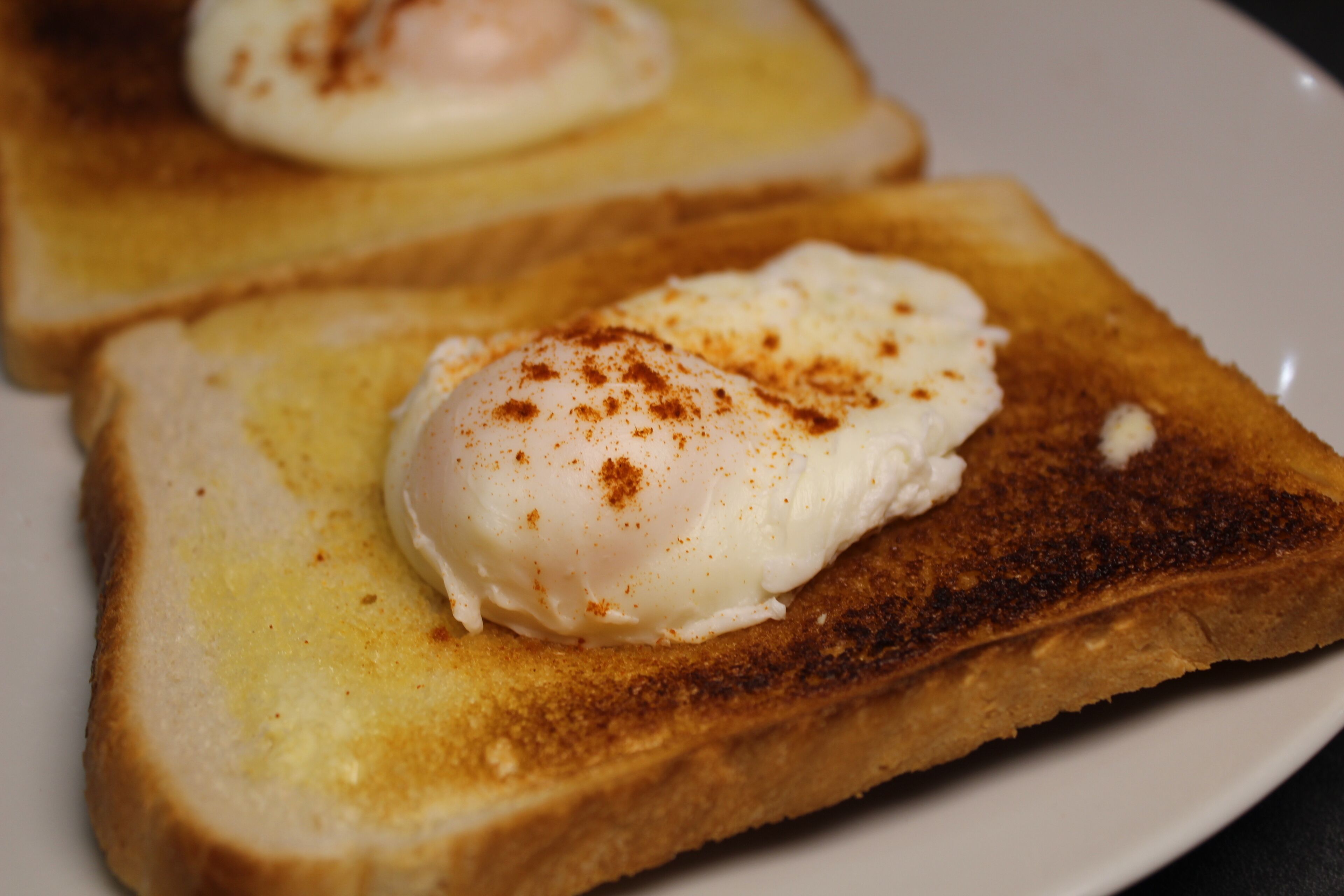 Two slices of toast with poached eggs and a sprinkle of seasoning.