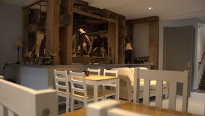 A dining area with a wooden table and white chairs, a staircase with a wooden railing, and a door in the background. - The Old Mill Bed & Breakfast (Biggar)