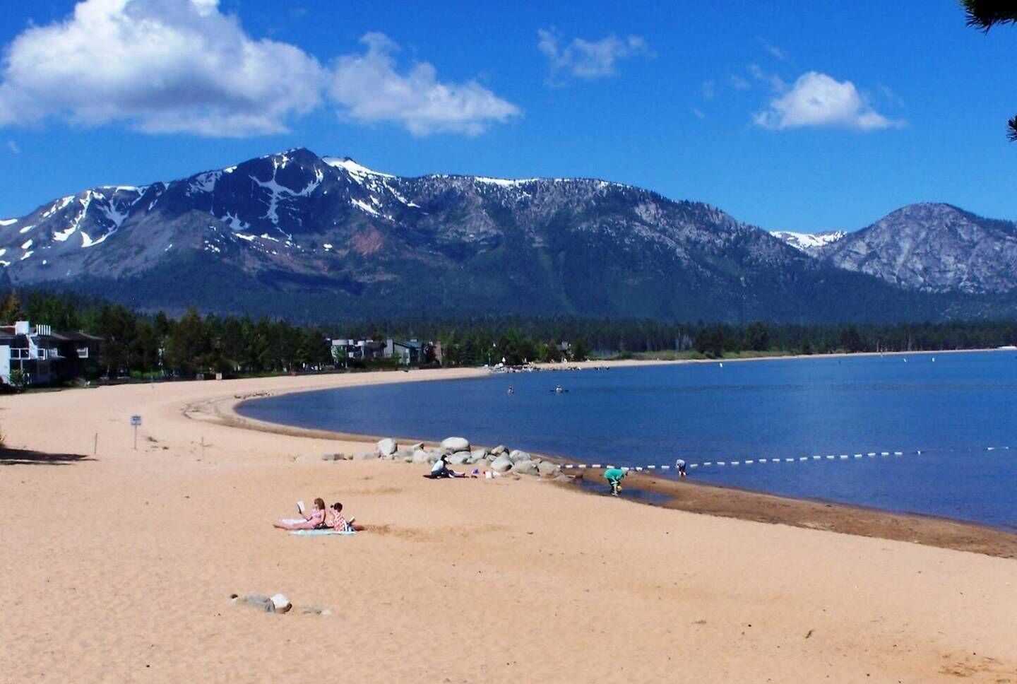 A beach with a mountain backdrop, clear skies, and a few people relaxing.