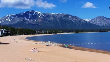 A beach with a mountain backdrop, clear skies, and a few people relaxing.