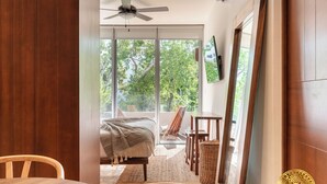 A bedroom with a bed, a ceiling fan, a TV mounted on the wall, and a view of the outdoors. - NHOA 209B Lux 1BR Pool View Aldea Zama (Tulum)