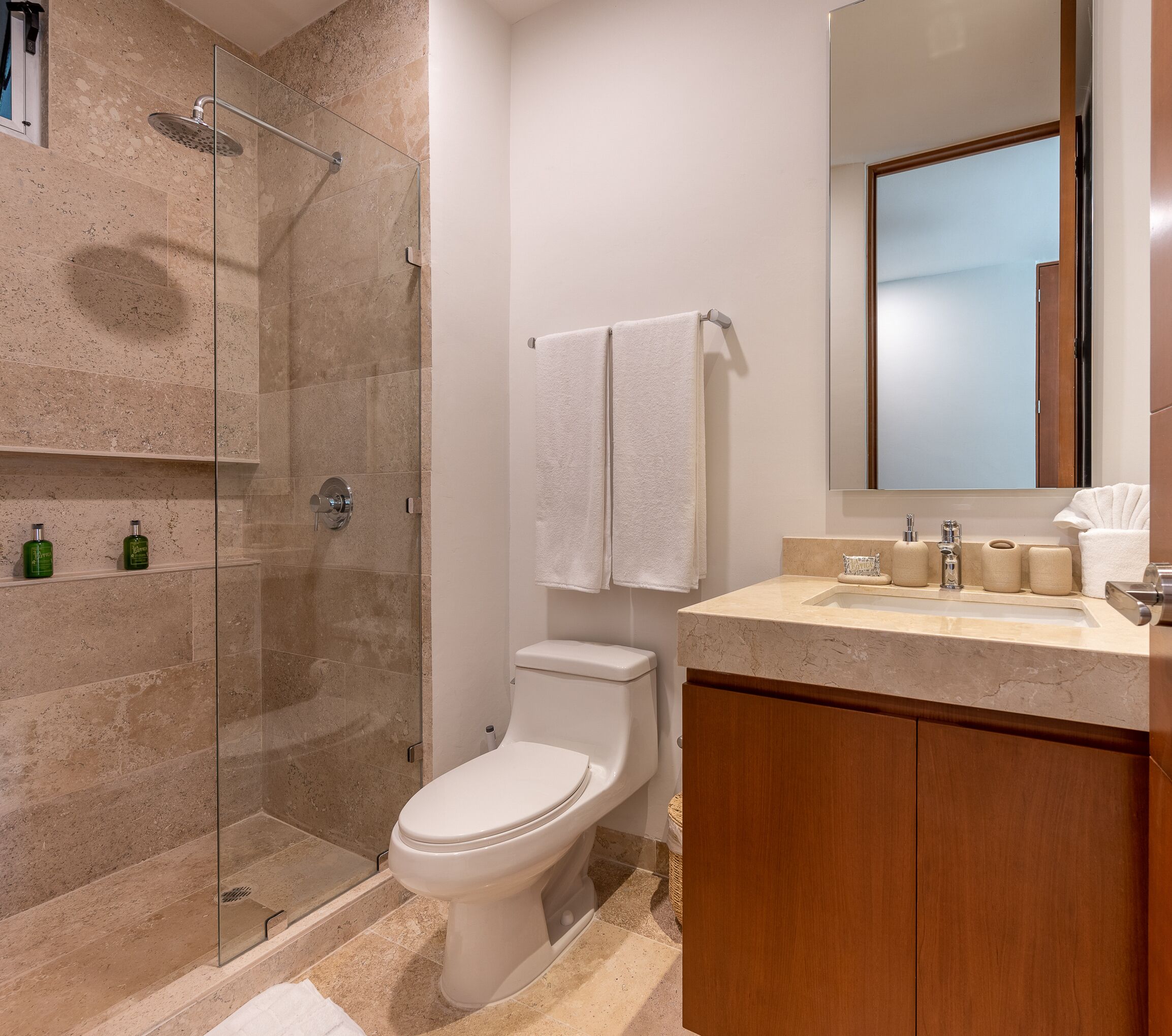 A bathroom with a glass-enclosed shower, a toilet, a sink with a mirror, and a wooden cabinet.