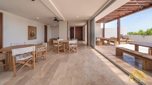 A spacious indoor area with wooden tables and benches, large windows, and a ceiling fan. - NHOA 209B Lux 1BR Pool View Aldea Zama (Tulum)