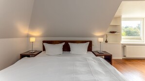 Un dormitorio con una cama grande, dos mesitas de noche, una ventana con vistas y un radiador.