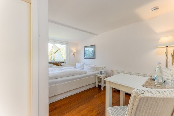 A bedroom with a bed, bedside table, lamp, and a view of the outside through a window.