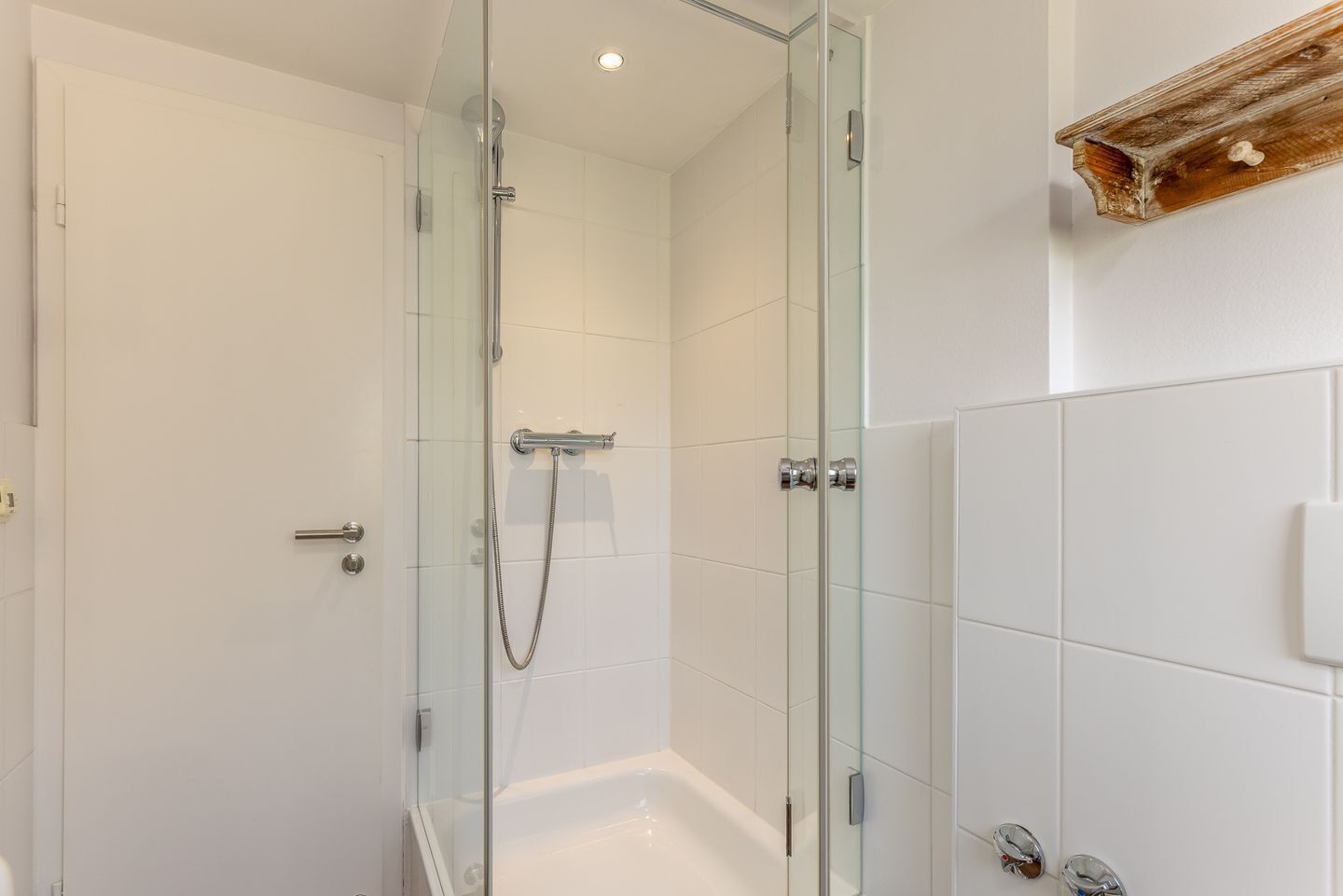 A modern bathroom with a glass-enclosed shower, a white bathtub, and a wooden shelf.