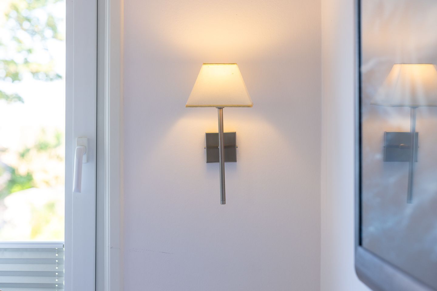 A wall-mounted lamp with a rectangular shade, a switch, and a light fixture on a plain wall.