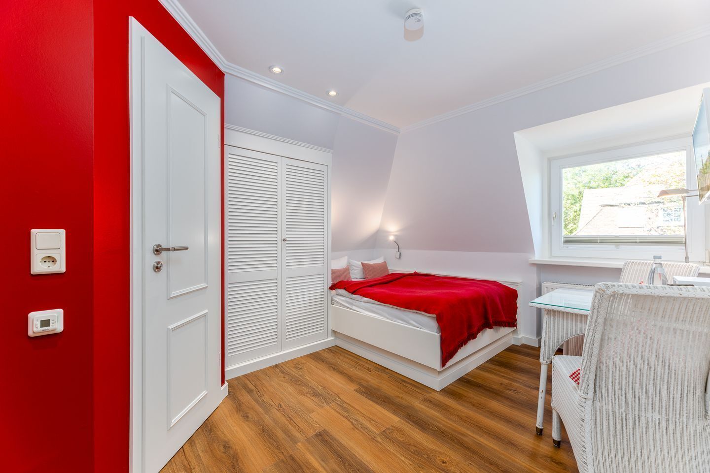 A bedroom with a bed, a desk, a chair, a wardrobe, and a window.
