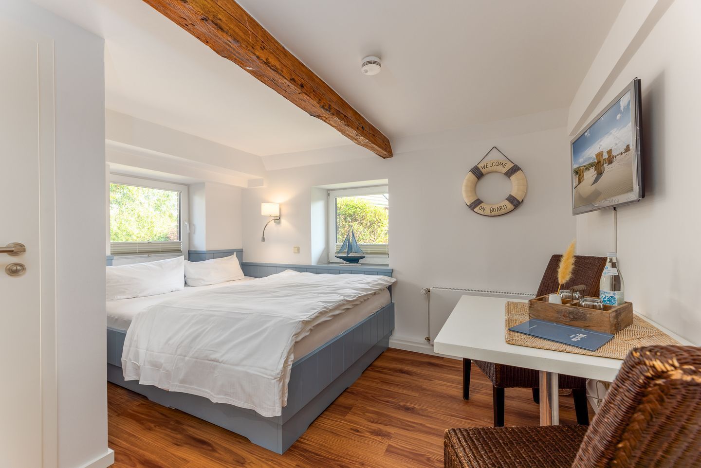 A bedroom with a bed, a desk, a chair, a wall-mounted TV, and a window.