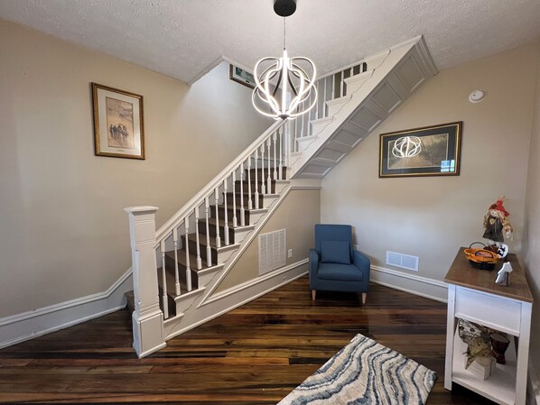 Un escalier avec des balustrades blanches, un fauteuil bleu et une petite table ornée d’objets décoratifs.