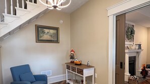 A living room with a blue armchair, a white console table, a patterned rug, and a staircase with white railings. - Shire-Southern-Comfort quiet 3-bedroom house w/WiFi and AC in heart of downtown  (Frankfort)
