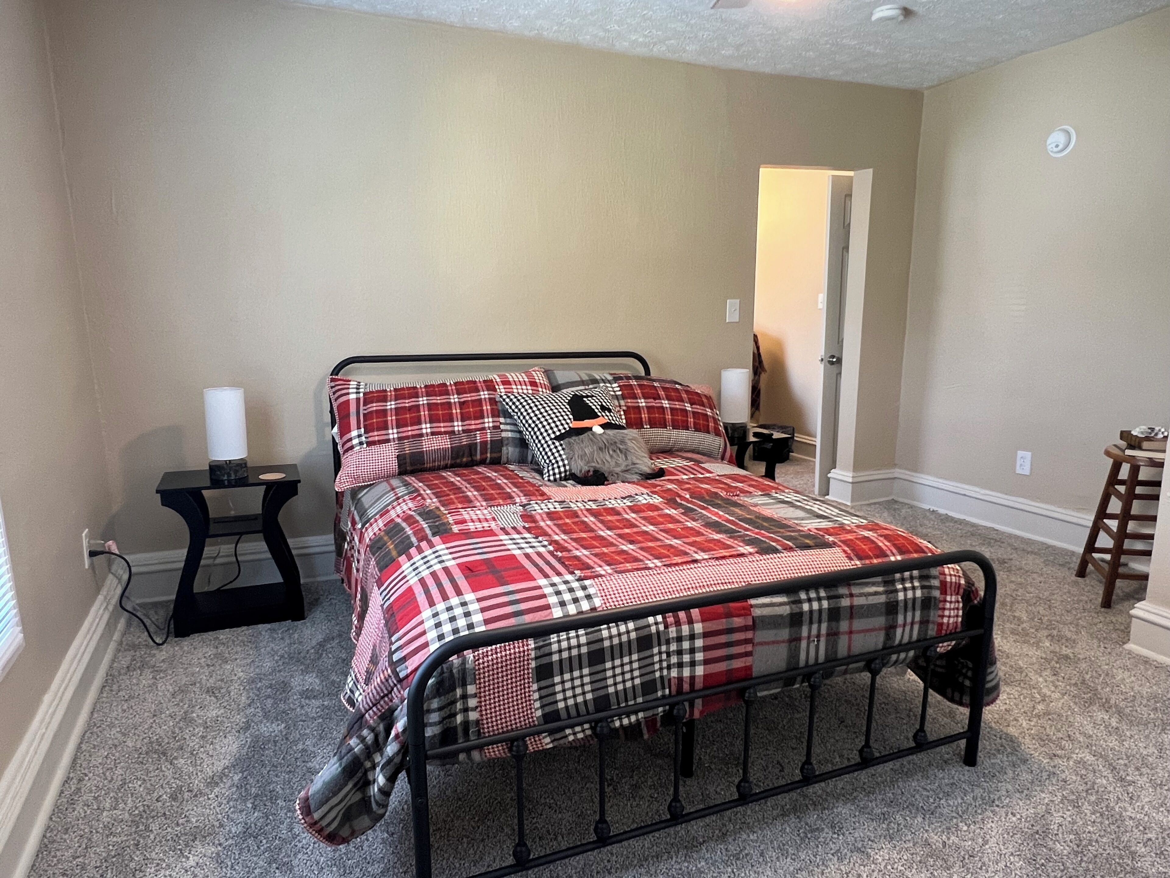 A bedroom with a bed, a nightstand, a lamp, and a chair.