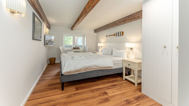 Un dormitorio con cama, mesitas de noche, armario y ventana con luz natural.