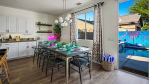 Una cucina moderna con mobili bianchi, una zona pranzo con un tavolo lungo e sedie, e vista su una piscina attraverso una porta scorrevole in vetro.