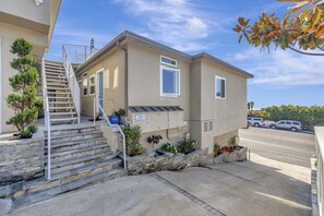 A two-story building with a stone staircase leading to the entrance, a mailbox, and a small garden area with plants. - Ocean VIEWS! Steps from Victoria Beach, Lux Design (Laguna Beach)