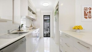 A modern kitchen with white cabinetry, a dishwasher, and a sink. There is a door leading to another room and a small plant on the counter. - Riviera Road Miami - 4BRM Dual Villa (Miami)