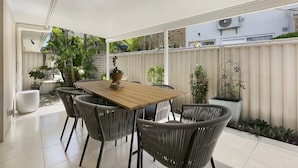 A covered patio area with a wooden table and wicker chairs, surrounded by potted plants and a white fence. - Riviera Road Miami - 4BRM Dual Villa (Miami)