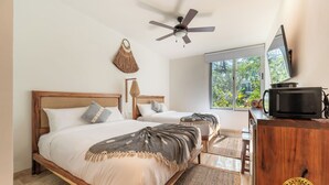 A bedroom with two beds, a ceiling fan, a large window, and a TV on a wooden dresser. - NHOA 209C Lux 1BR Pool View Aldea Zama (Tulum)