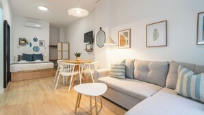 Un salon moderne comprenant un canapé, une table à manger avec des chaises, un téléviseur fixé au mur et une petite table sur laquelle est posée une plante.