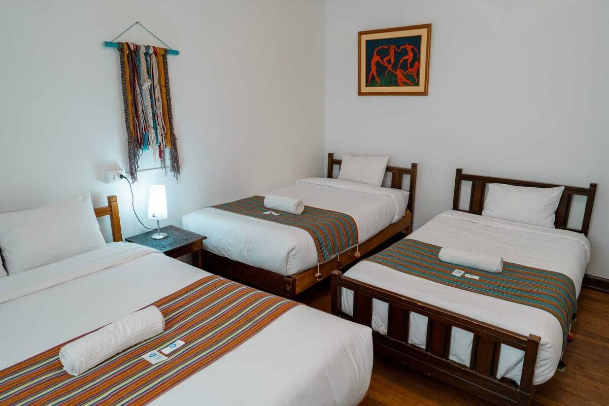 A hotel room with three single beds, a wooden headboard, a wall-mounted artwork, and a hanging tapestry.