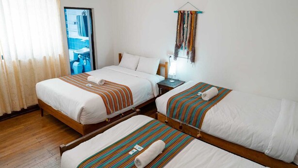 Ein Hotelzimmer mit zwei Betten, Holzboden, Badezimmer mit Spiegel und Wanddekoration.