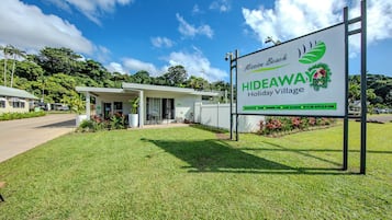 A sign for Mission Beach Hideaway Holiday Village with a white building and a grassy area in front.