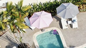 A swimming pool with multiple lounge chairs and umbrellas, surrounded by palm trees. - Hideaway Mission Beach Village (Mission Beach)