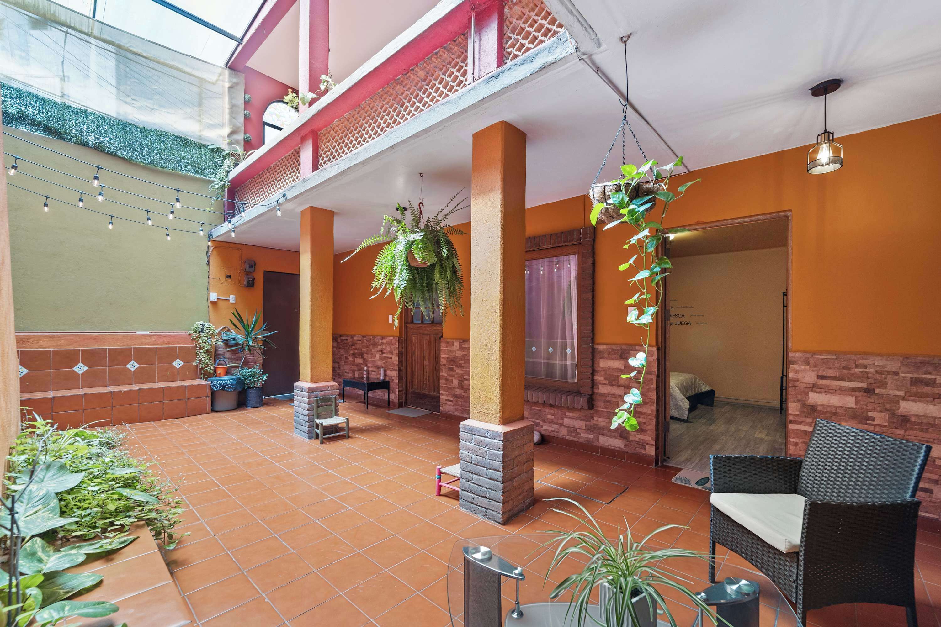 Amplo espaço interno com piso em azulejos, vários conjuntos de assentos e plantas penduradas.