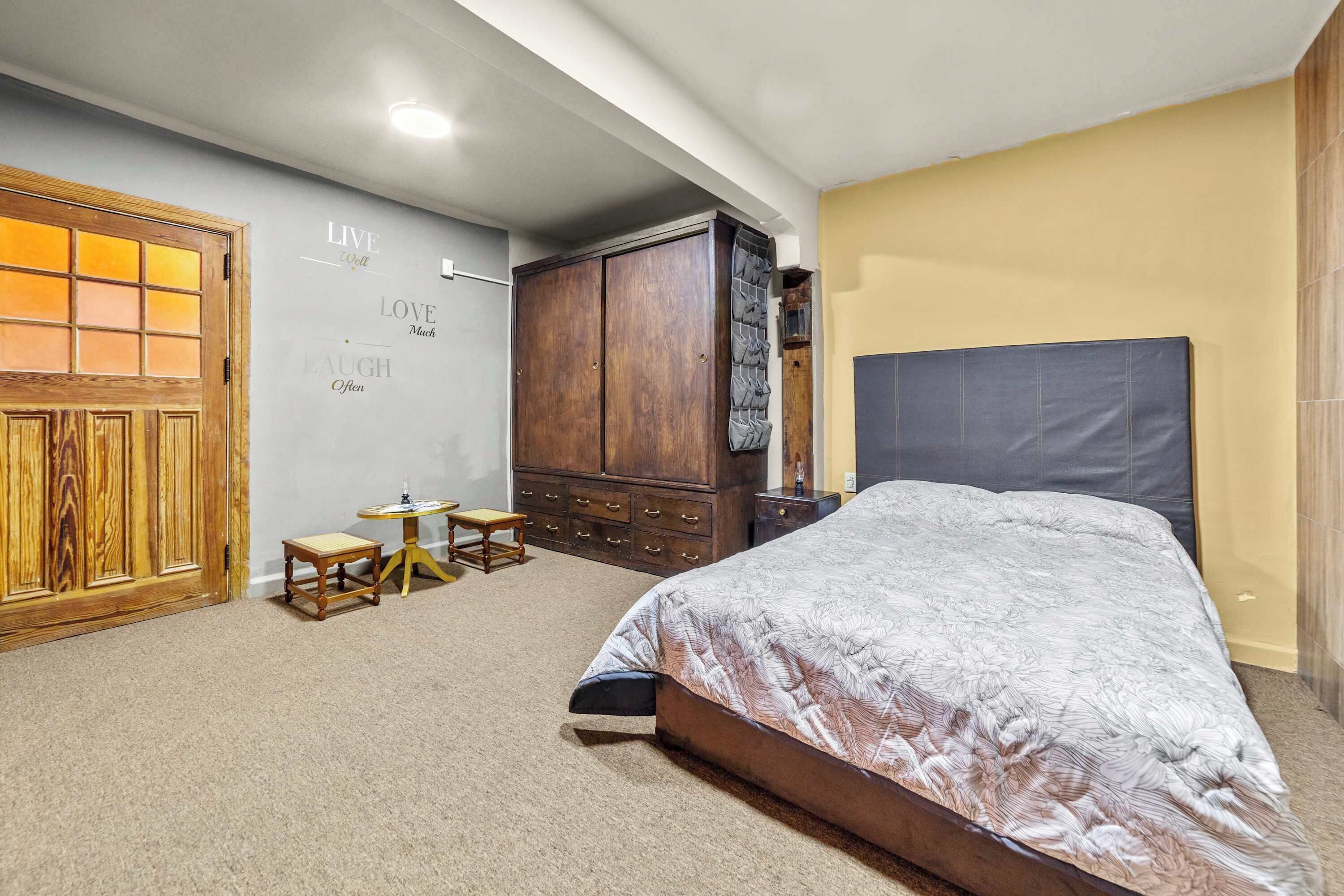 A bedroom with a bed, a wooden wardrobe, a small table, and a wall with motivational phrases.