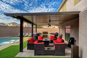 Un patio al aire libre con mobiliario de mimbre, una parrilla y una piscina.