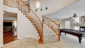 A spacious living area with a wooden staircase, a pool table, and a chandelier.