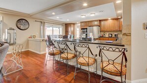 A modern kitchen with wooden cabinets, a stainless steel refrigerator, and a bar area with bar stools.
