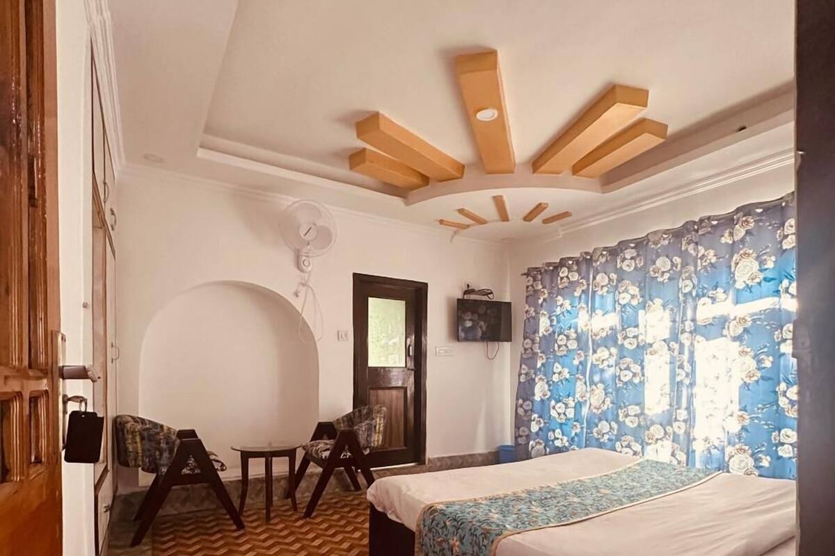 A room with a herringbone floor, a bed with a floral bedspread, a wooden ceiling with exposed beams, a fan, and a door with a wooden frame.