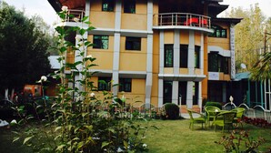 A multi-story building with a yellow facade, balconies, and a garden area with chairs. -  Barzam Lake View Resort (Srinagar)