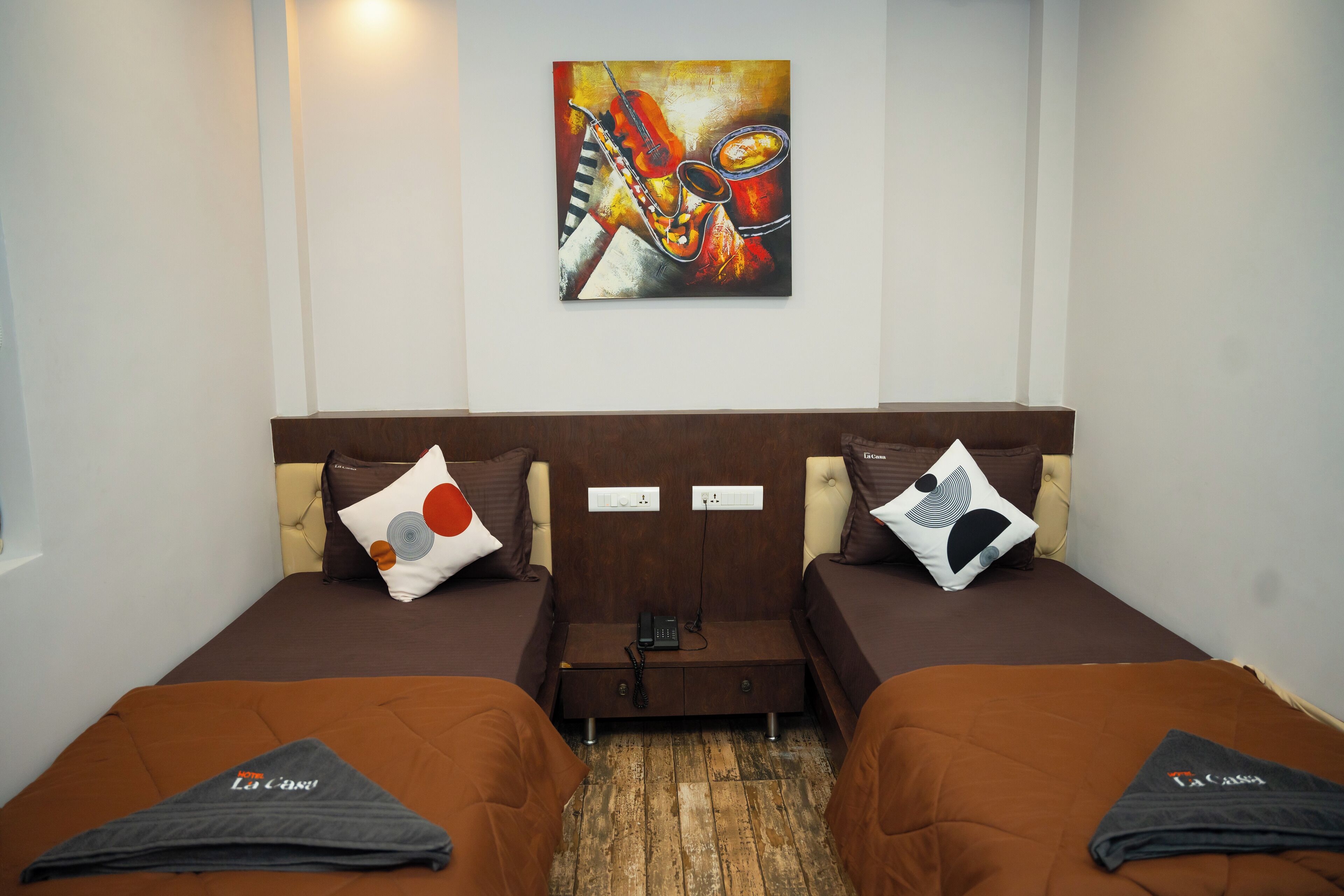 A hotel room with two beds, a wooden floor, a painting on the wall, and a small table between the beds.